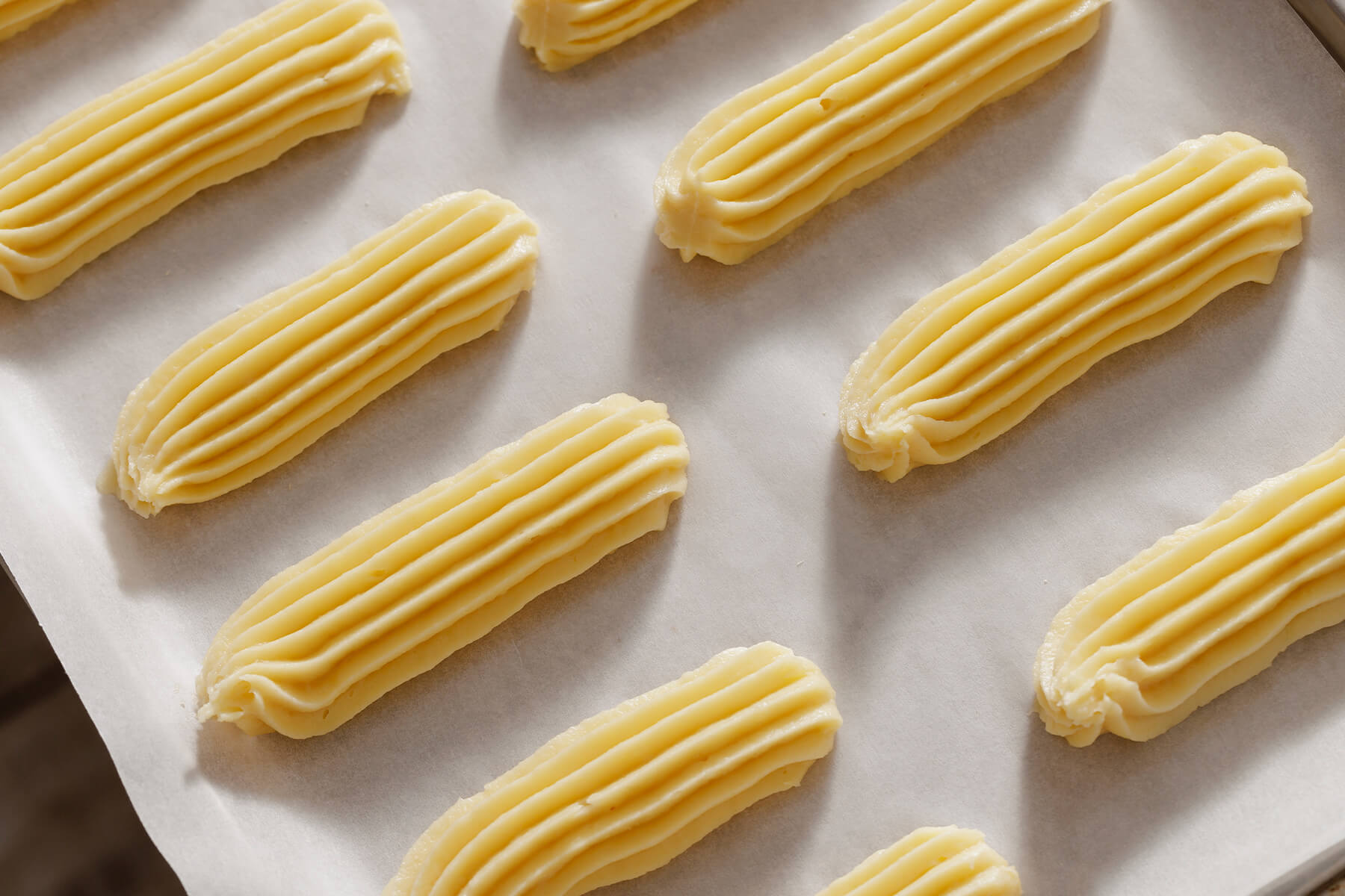 Rohe Éclair-Streifen mit glänzender Oberfläche und tiefen Längsrillen auf Backpapier