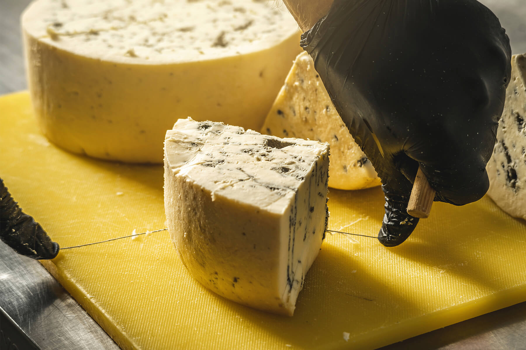 Von einem geteilten Gorgonzola-Laib wird mit dem Draht ein Keil abgetrennt, die Schnittfläche hell und glatt mit blaugrauen, bröckeligen Schimmelnestern
