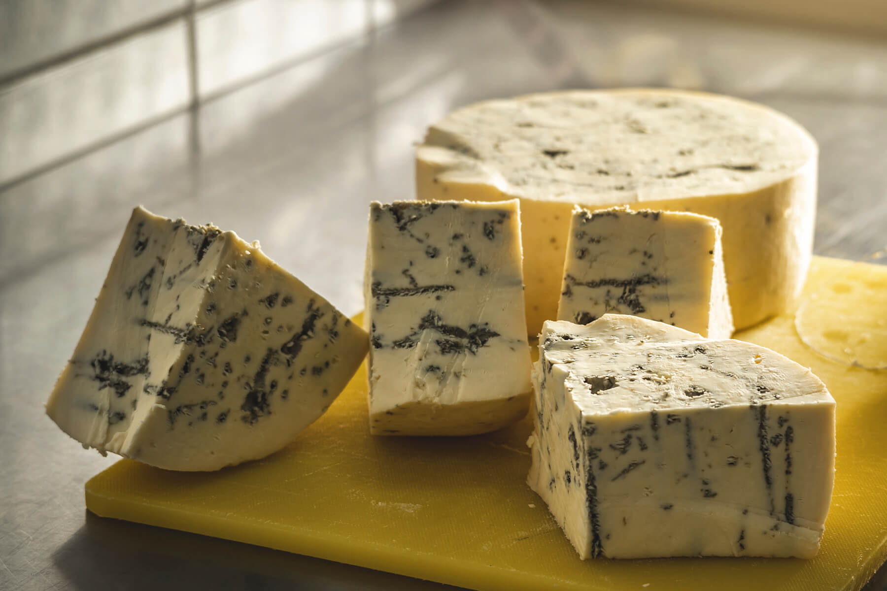 Dicke Gorgonzola-Keile und der Rest des Laibs auf einem gelben Schneidebrett, cremiger Teig mit dunklen grünlich-blauen Adern und Schimmelnestern