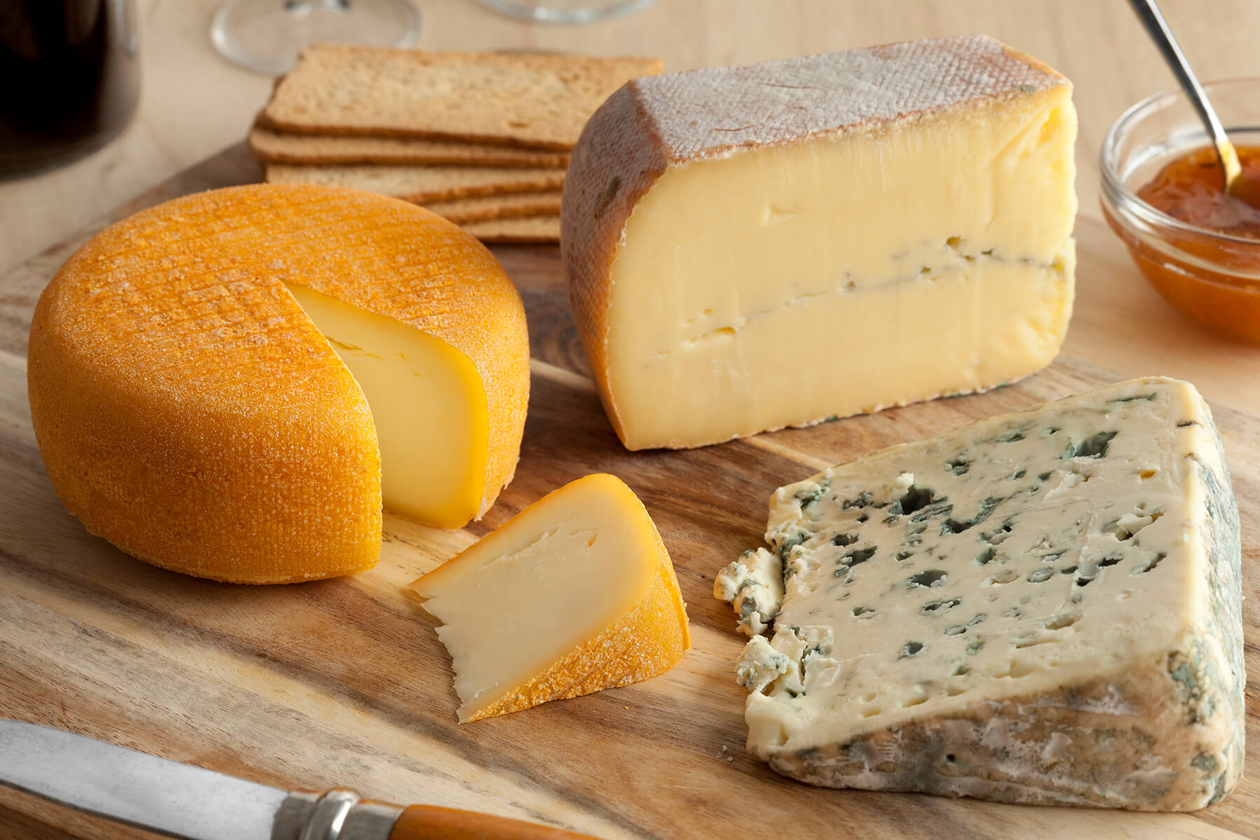Holzbrett mit einem Block Morbier mit schwarzem Aschestreifen in der Mitte, einem runden Rotschmierkäse mit herausgeschnittenem Stück und einem Keil Blauschimmelkäse