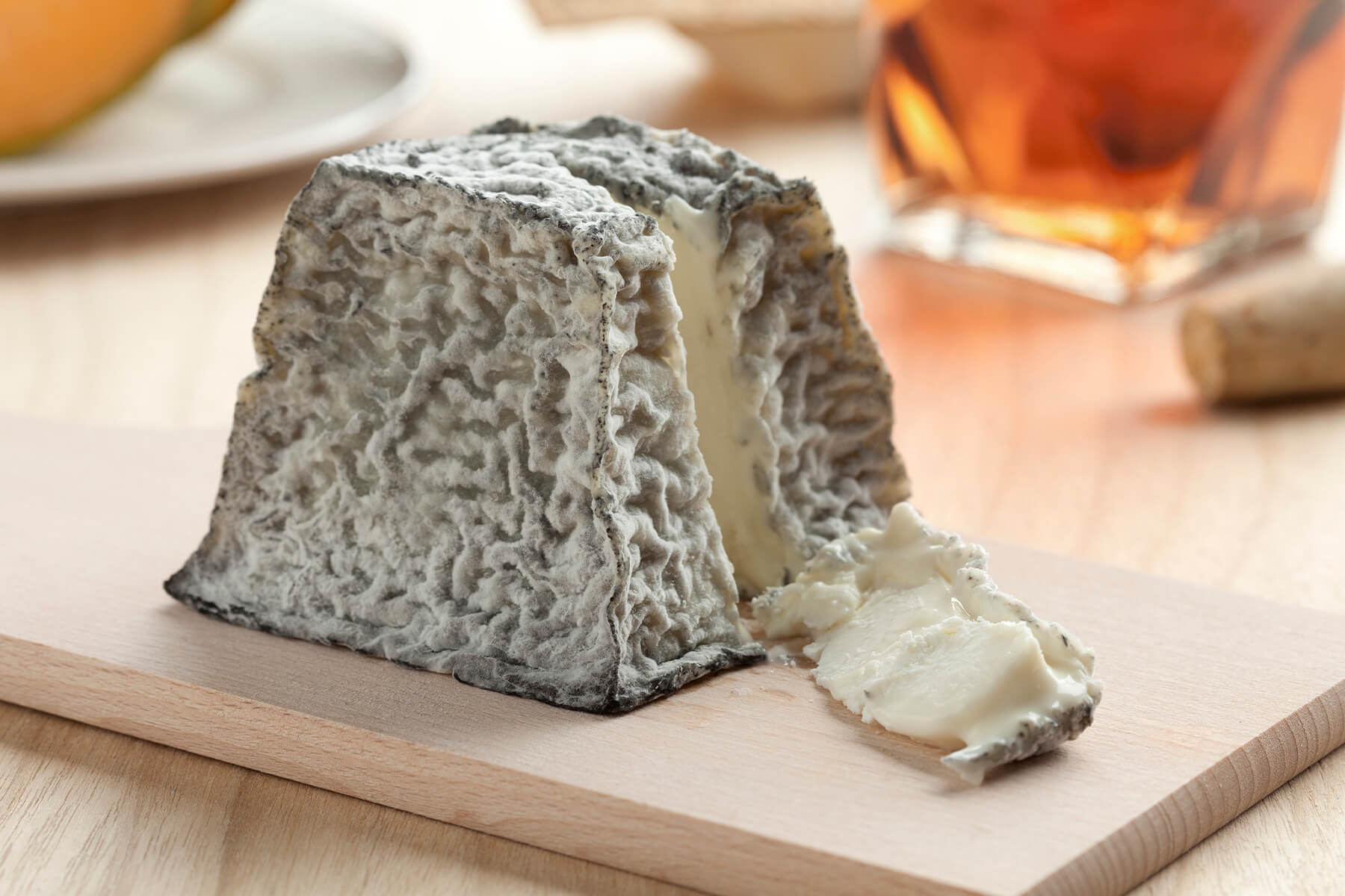 Ziegenkäse in Form einer abgeschnittenen Pyramide mit dunkler Ascherinde, ein Stück liegt daneben und zeigt den schneeweißen Teig